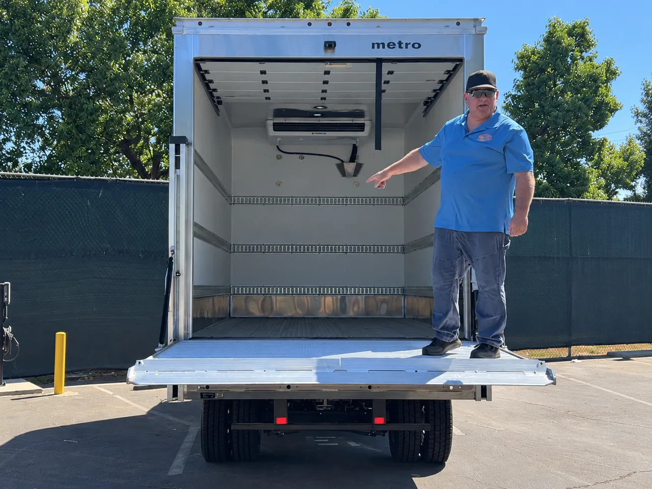 Escondido School District staff member in a blue polo standing on the lowered liftgate of a RIZON electric box truck, pointing to the cooling unit inside the open cargo box